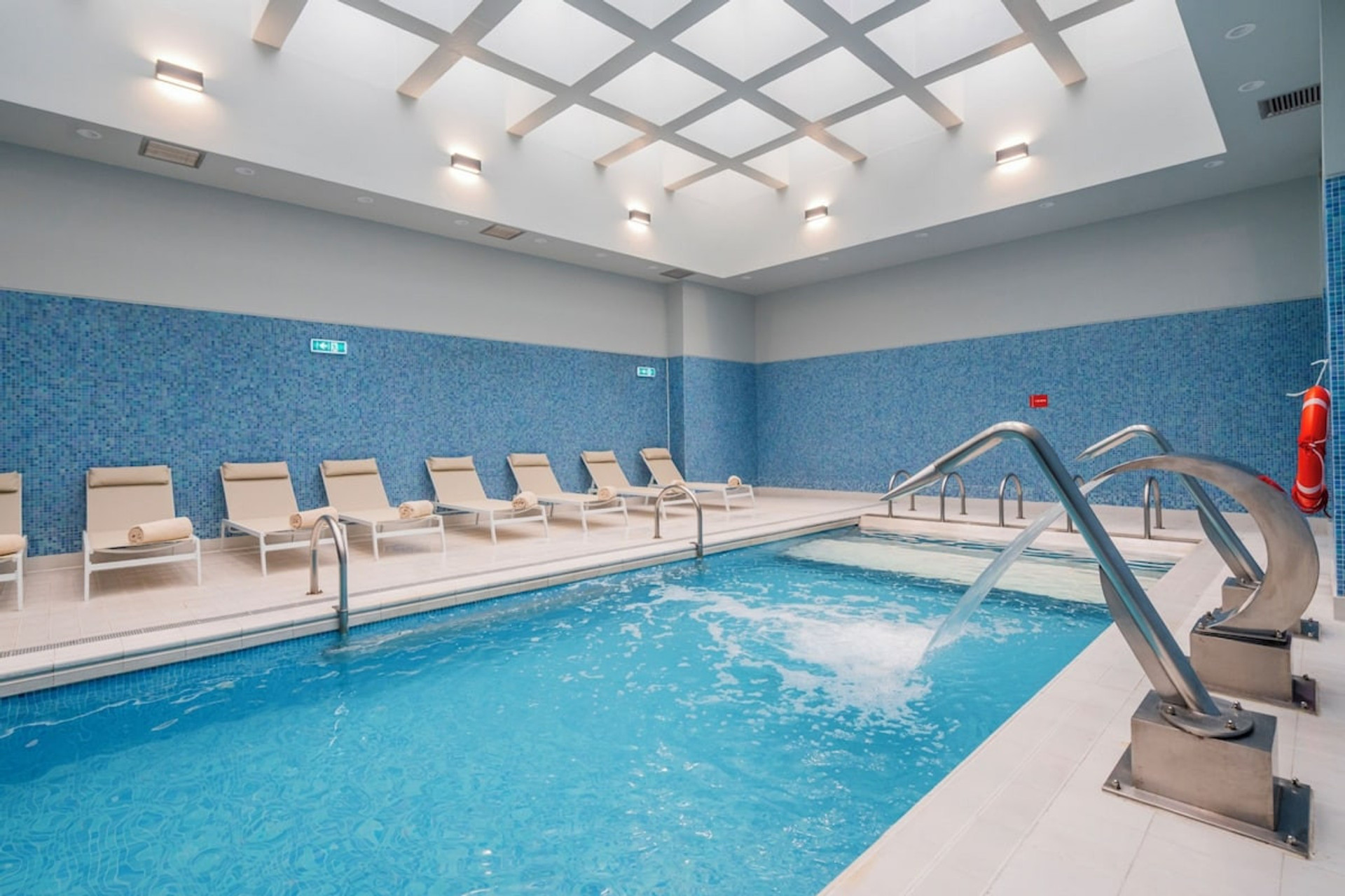 Heated indoor pool with water features and seating area