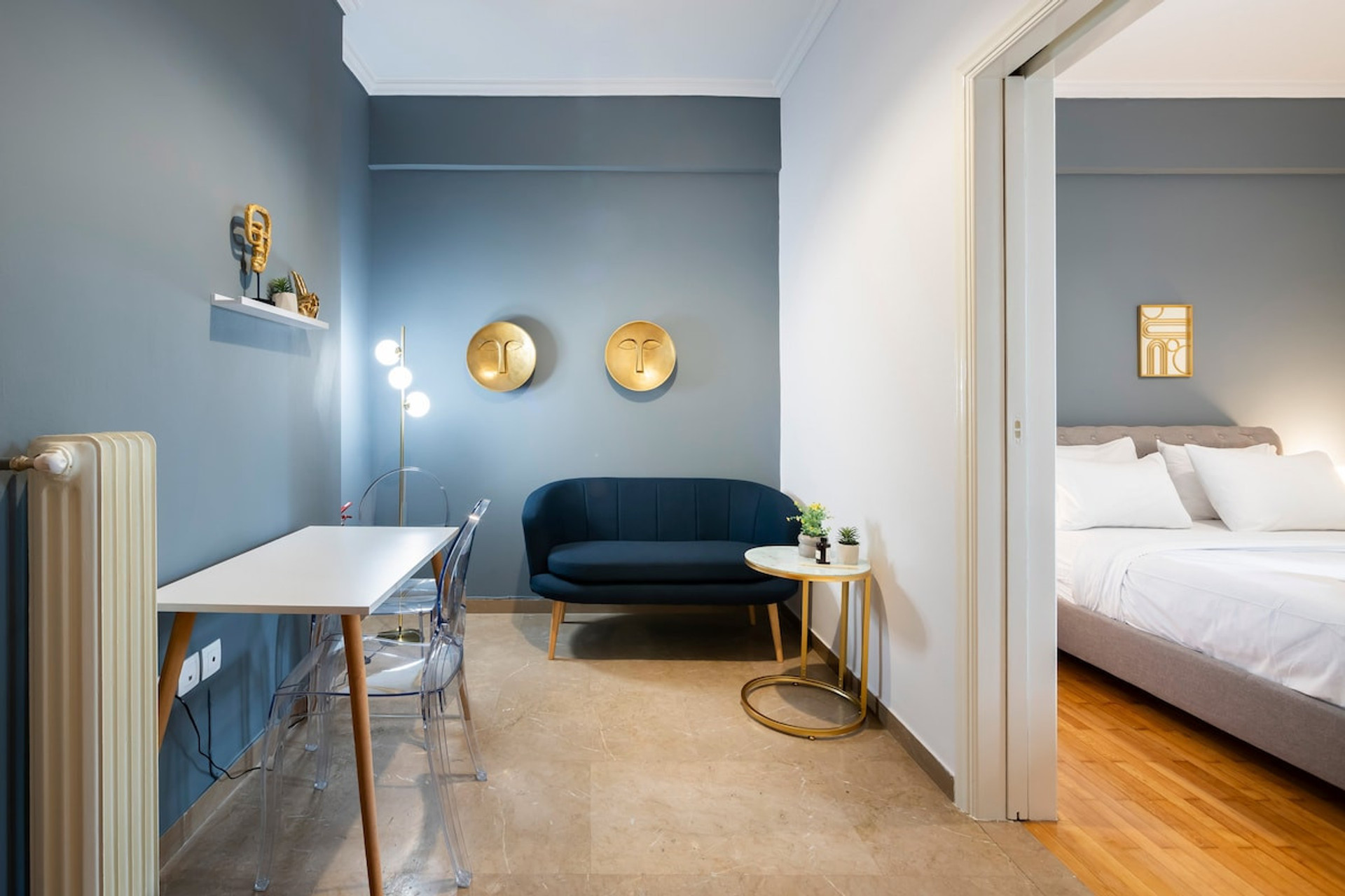 A cosy and stylish living space with a modern blue accent wall, a comfortable sofa, and a sleek desk area. Warm lighting and elegant decor create a relaxing atmosphere, seamlessly connected to a serene bedroom with soft bedding. Perfect for unwinding