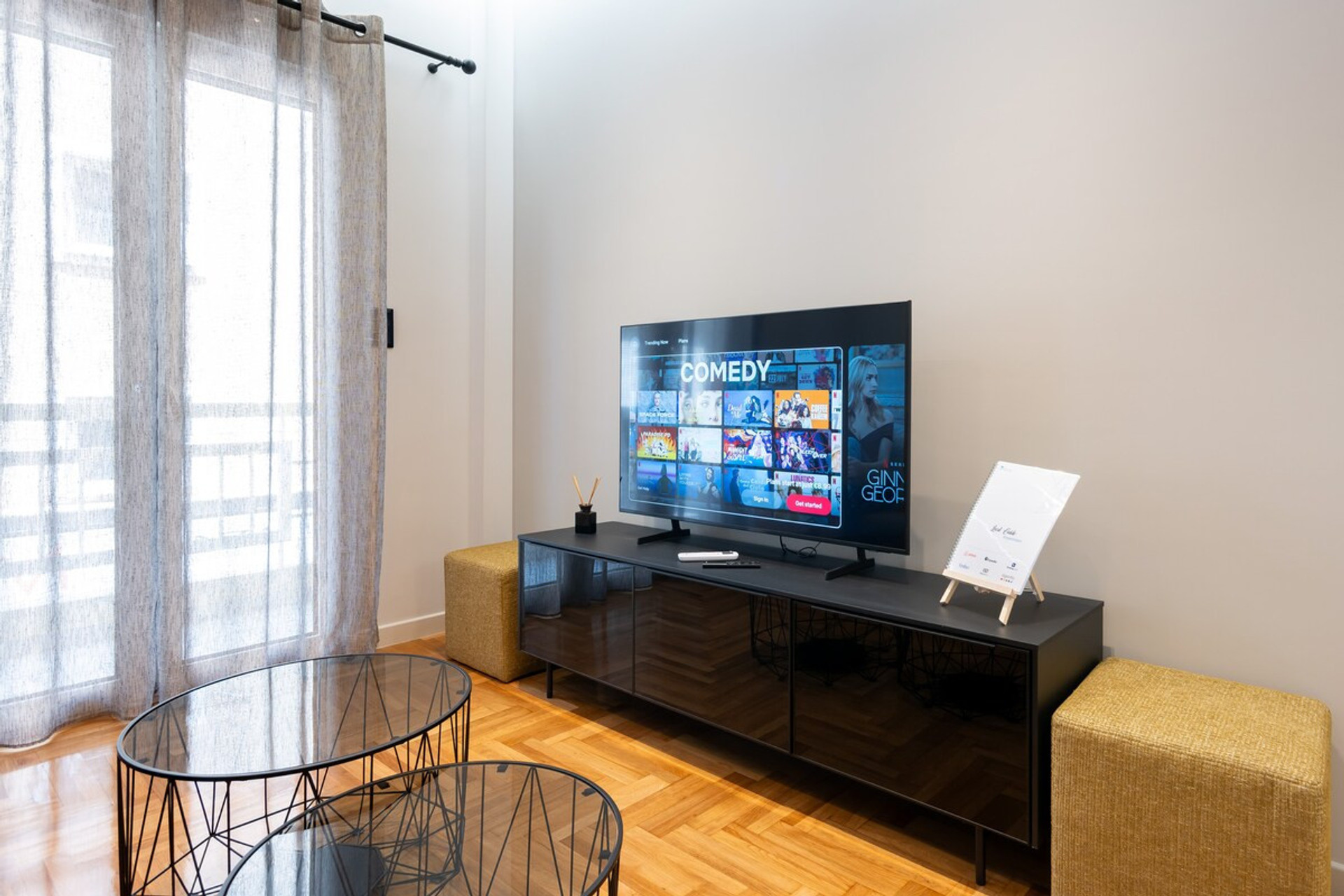 A cosy, light-filled living space featuring a sleek TV setup perfect for entertainment. The modern furnishings, including a stylish glass coffee table and comfortable seating, create a welcoming atmosphere. Ideal for relaxing after a day of exploring