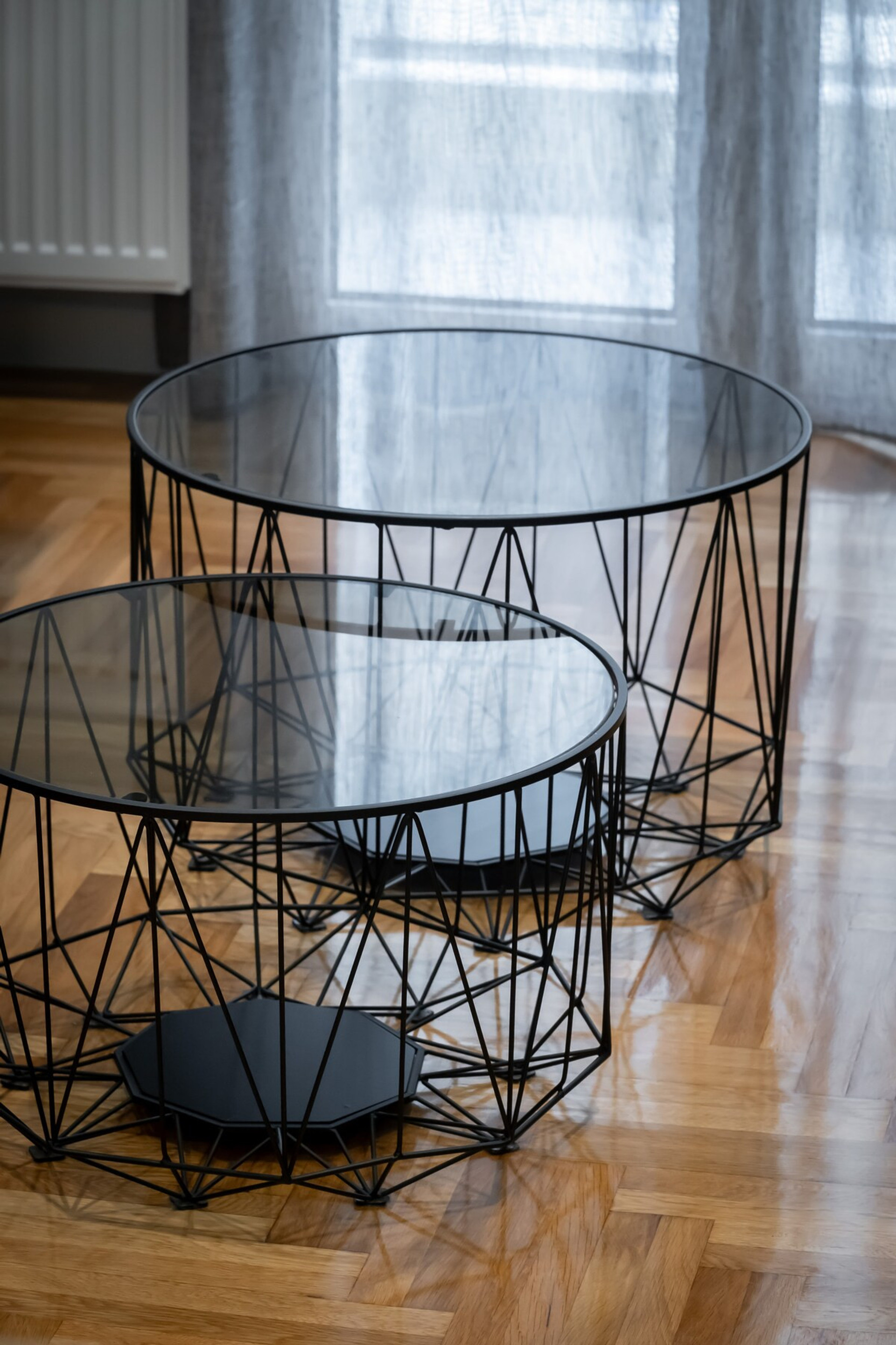 Elegant and modern glass-topped coffee tables with intricate geometric metal frames, set against a polished wooden floor. A stylish addition to any living space, perfect for creating a cosy and contemporary atmosphere.