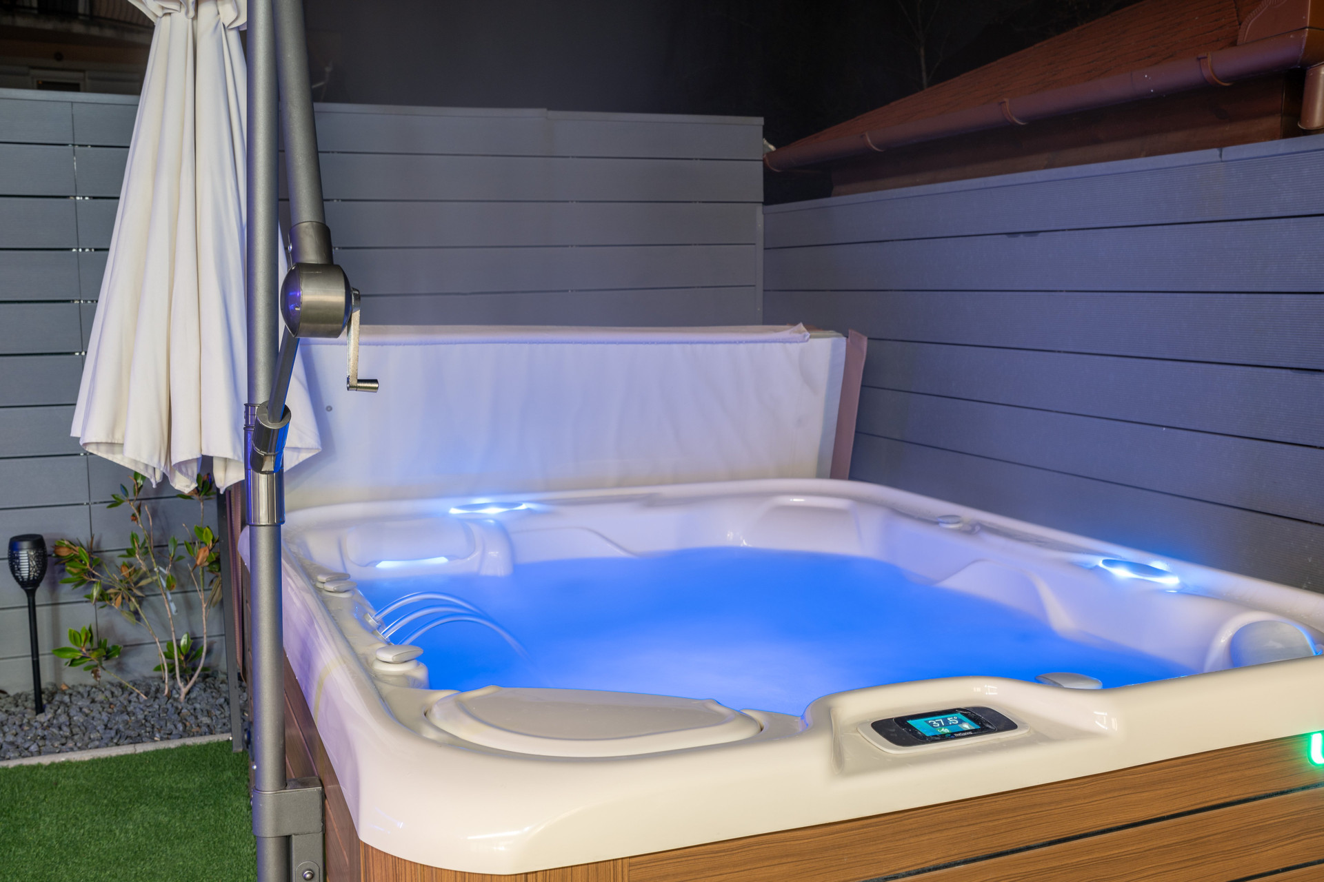Premium 6-person HotSpring Highlife hot tub in the garden, equipped with a parasol. It is operational year-round, offering you the perfect private relaxation every single day.