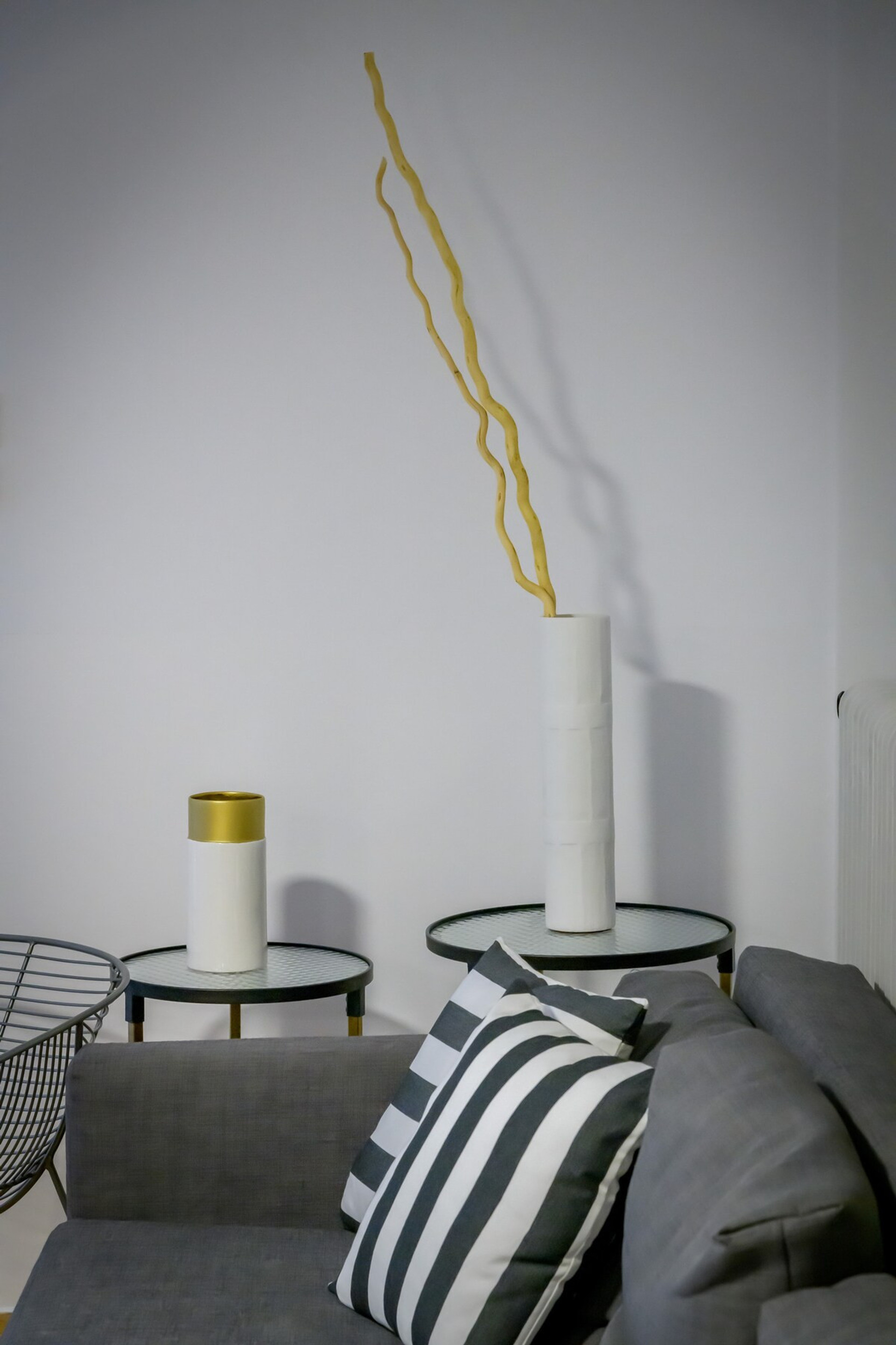 Elegant and modern living area featuring a chic grey sofa adorned with a striped cushion. Minimalist decor includes sleek tables with contemporary vases, adding a touch of sophistication. Perfect for unwinding in a serene and tasteful environment.