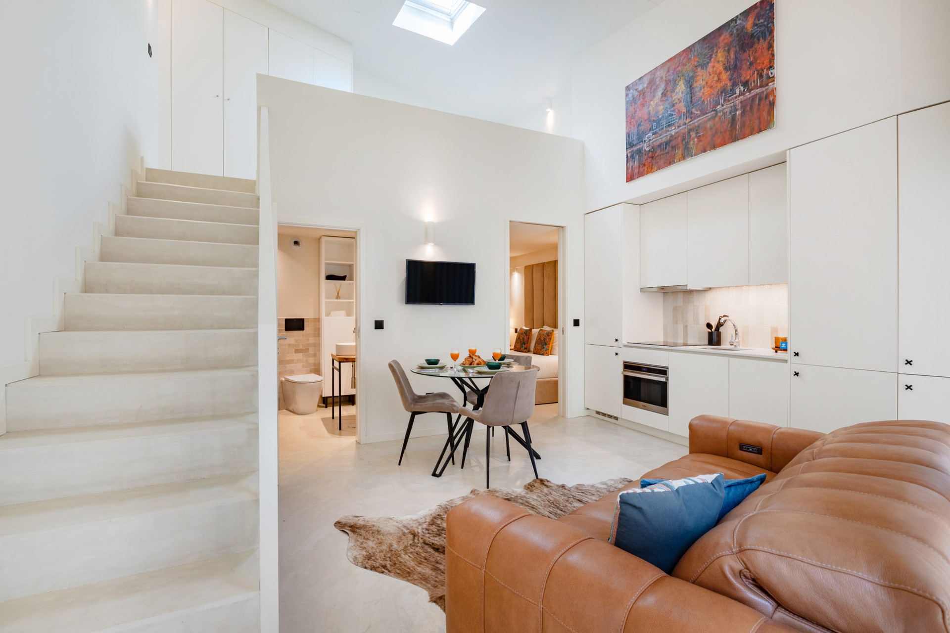 Living area with a leather sofa, TV, kitchenette, and dining table. Staircase leading to the mezzanine.