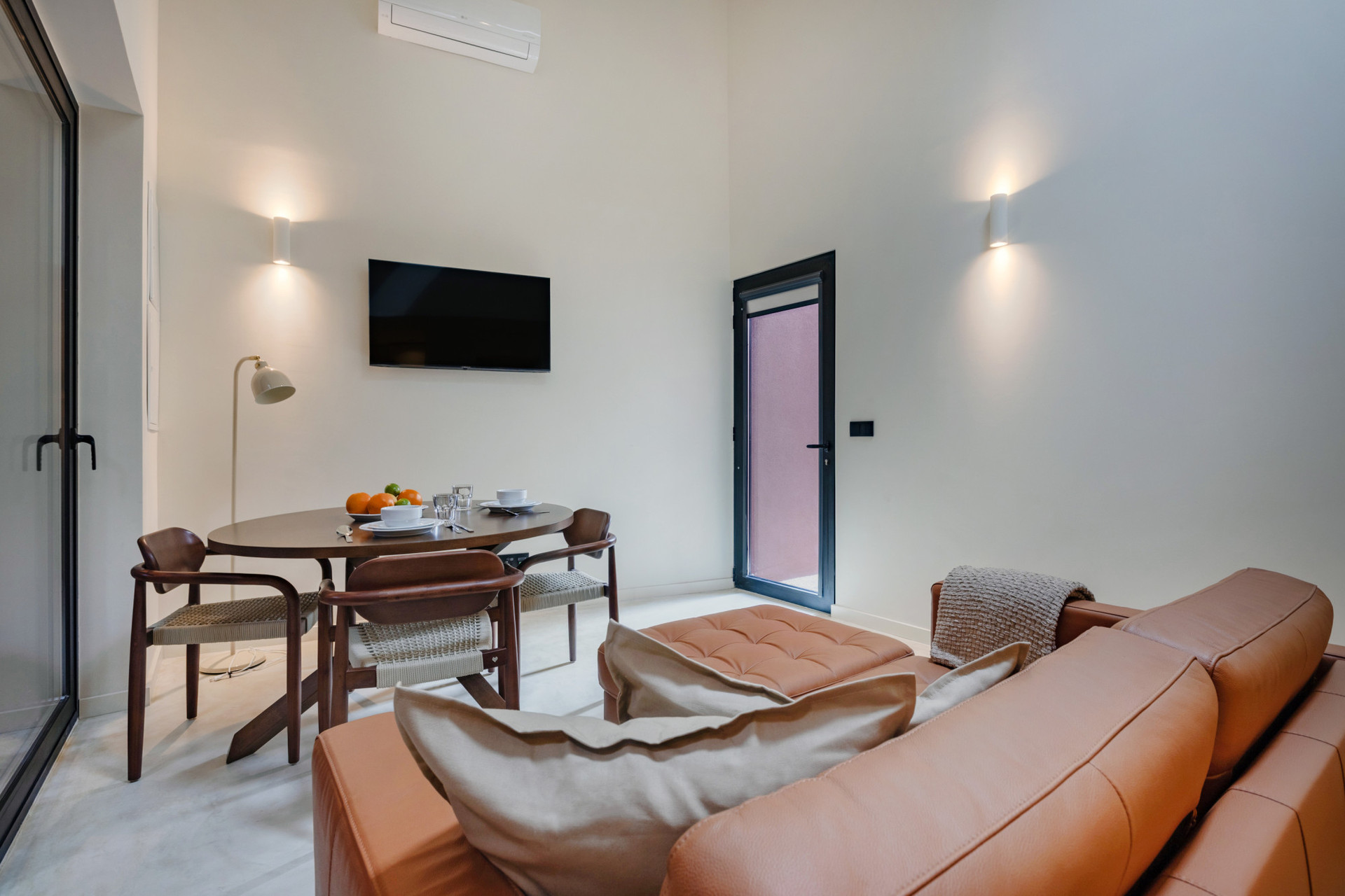Simple, yet comfortable living area with AC, an elegant leather sofa, TV and dining table (that doubles as a working space). Staircase to the mezzanine bedroom.