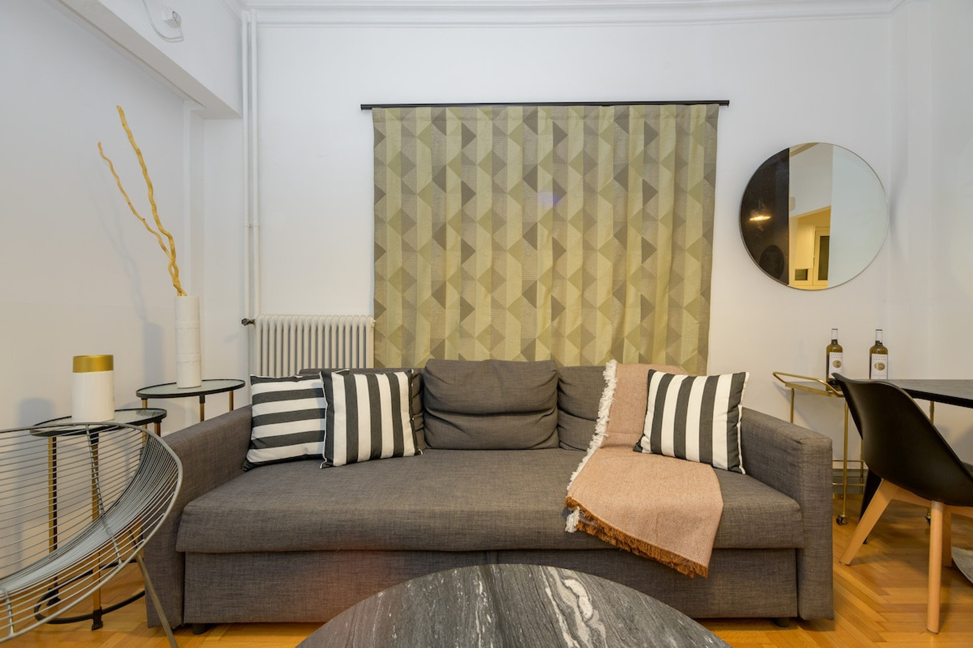 Charming and inviting living room featuring a plush grey sofa adorned with stylish striped cushions. A modern round mirror and chic side tables add elegance, while warm lighting creates a cosy atmosphere perfect for relaxation.