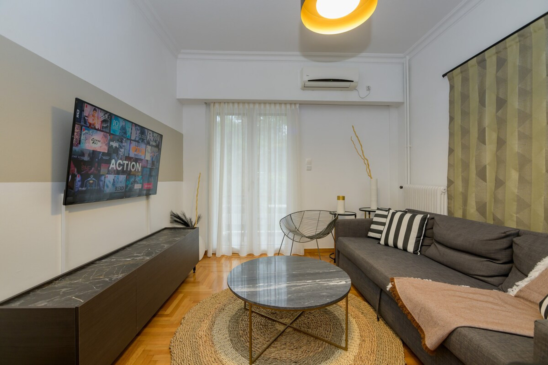 Charming and modern living room with a sleek wall-mounted TV, stylish grey sofa, and chic cushions. A contemporary round coffee table and inviting rug complete the cosy ambiance. Perfect for relaxation and unwinding in a delightful setting.