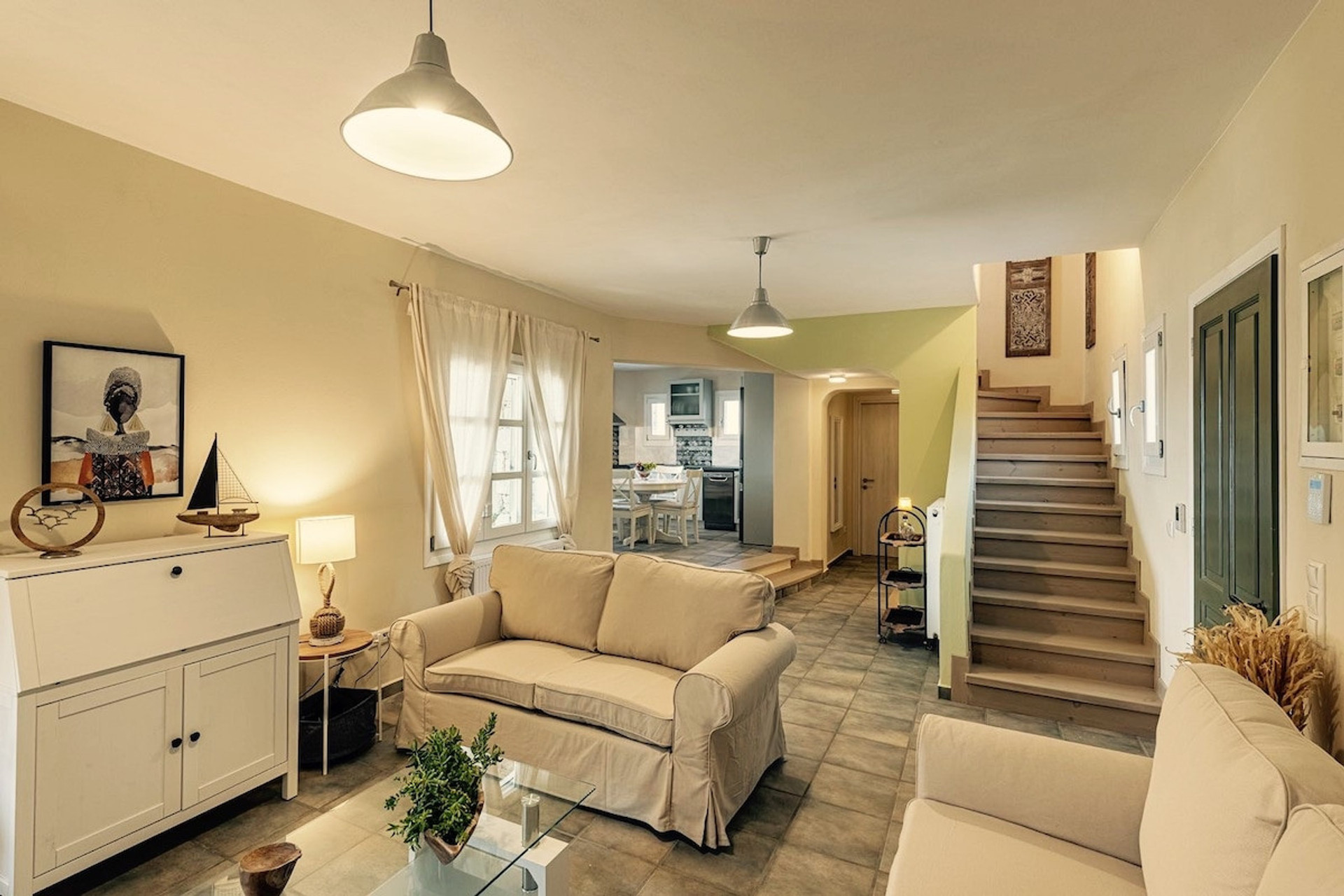 This elegant Mediterranean abode captivates with its harmonious neutrals and thoughtful design. Sun-kissed walls complement the rustic stone flooring, while the tailored slip-covered sofa invites lingering conversations.