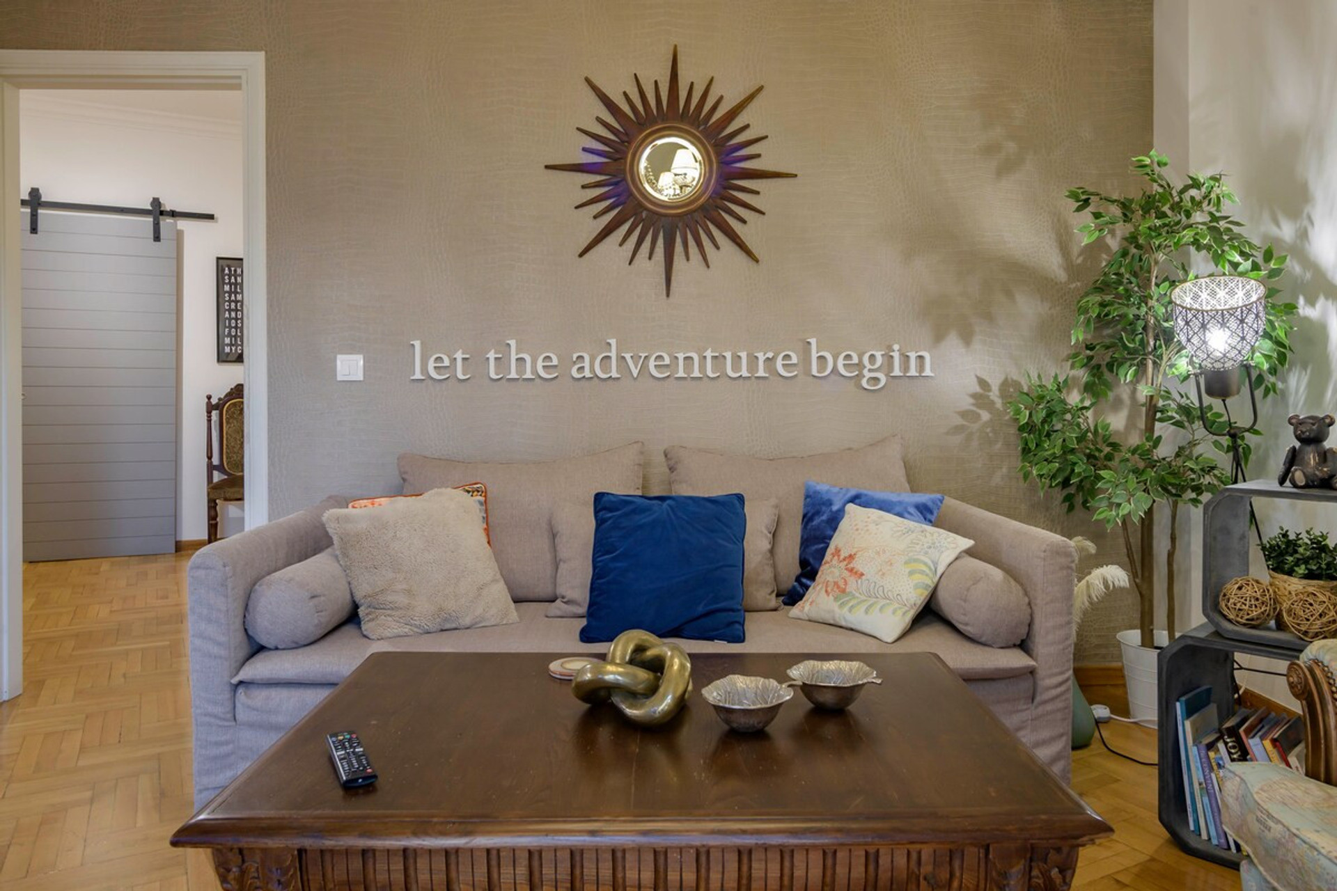Cosy living room with a charming wall design that invites adventure. Features a plush sofa adorned with colourful cushions, a stylish coffee table, lush greenery, and warm lighting—perfect for relaxation or planning your next journey.