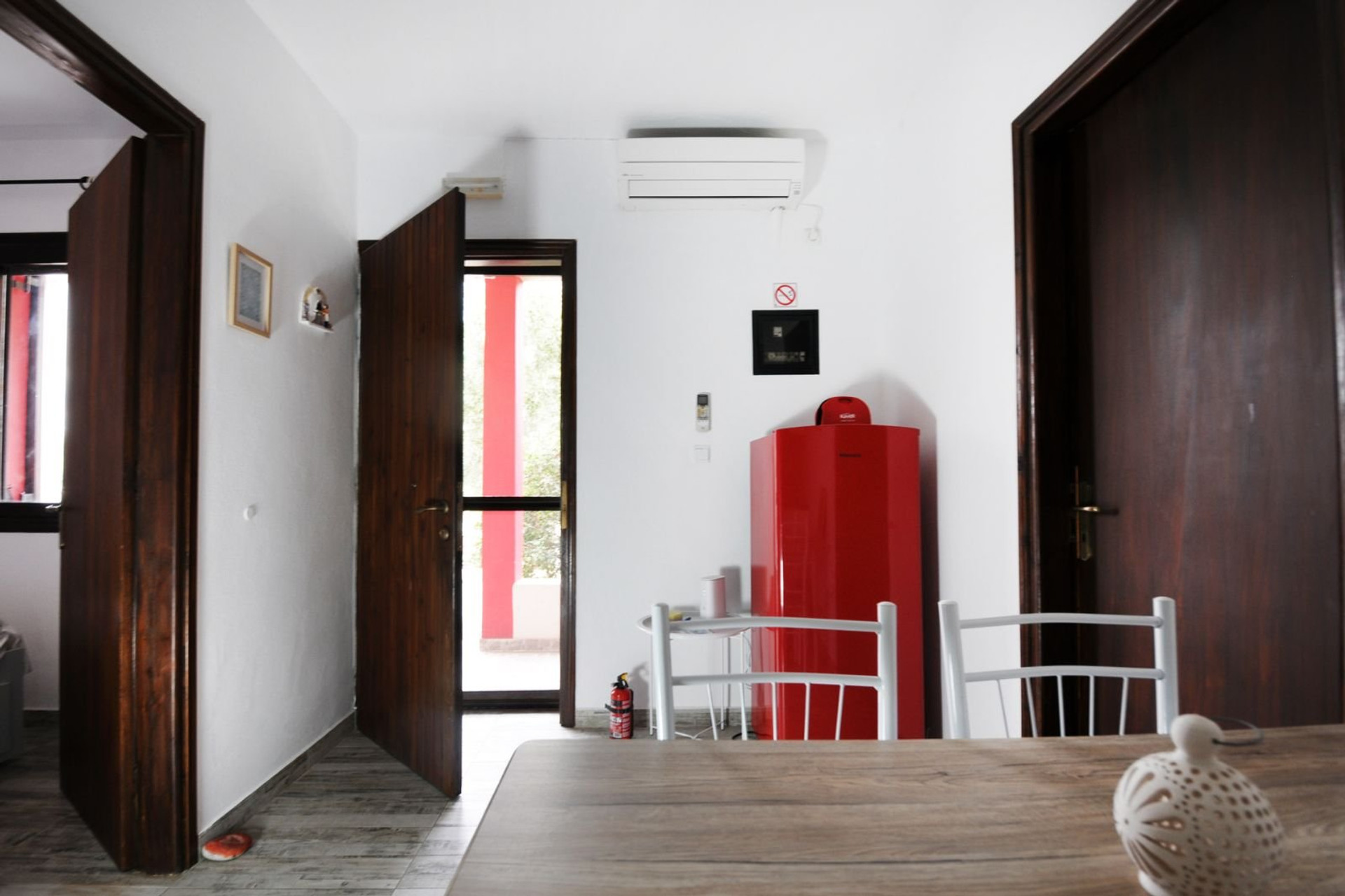 A bright and welcoming living area with clean lines, wooden accents, and practical amenities, including a red refrigerator and air conditioning — ideal for comfortable everyday living.