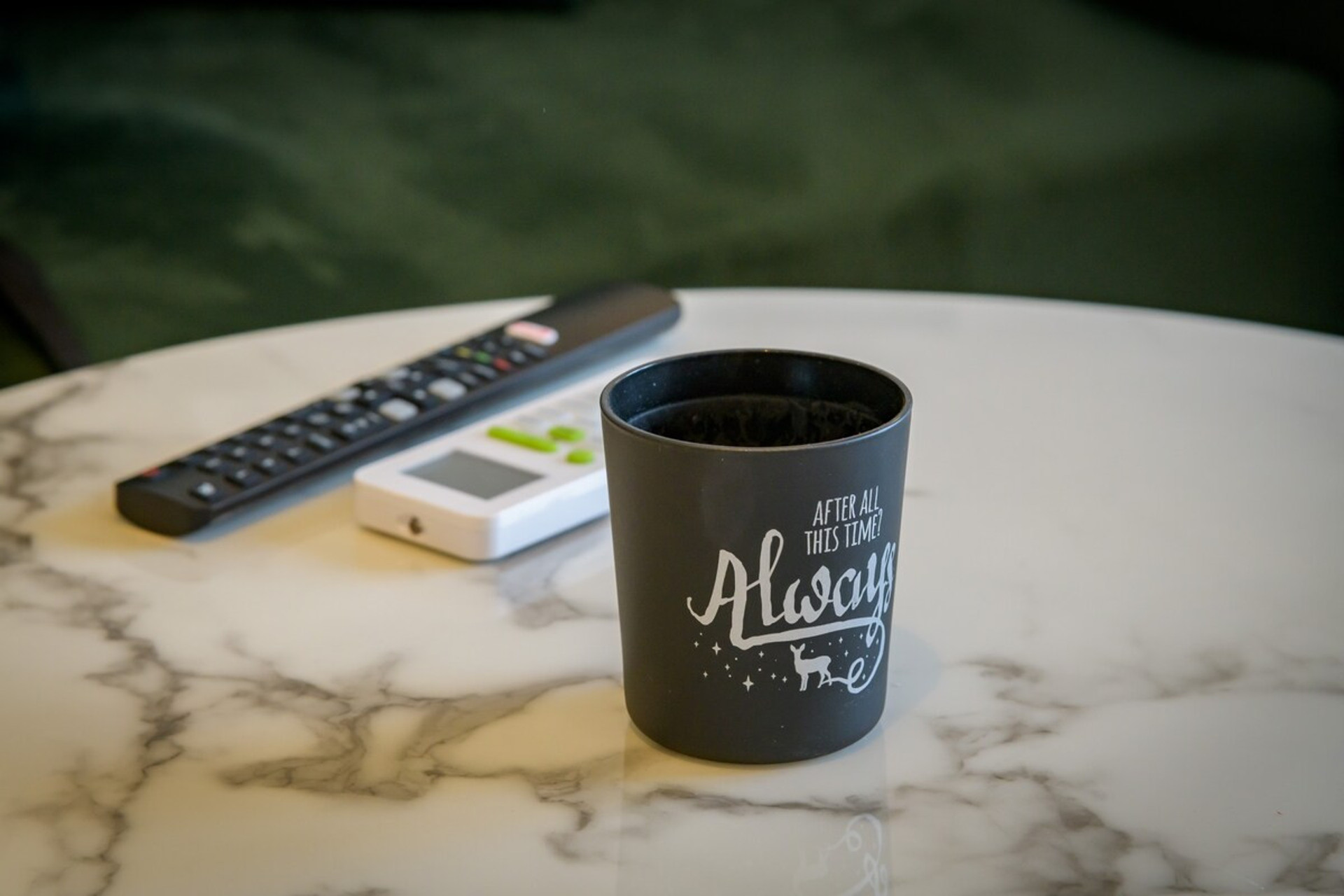 Cosy and inviting, this marble-top table features a charming candle holder with "After all this time? Always" inscribed, adding a touch of warmth and elegance. Ideal for relaxing evenings with remote controls conveniently at hand.