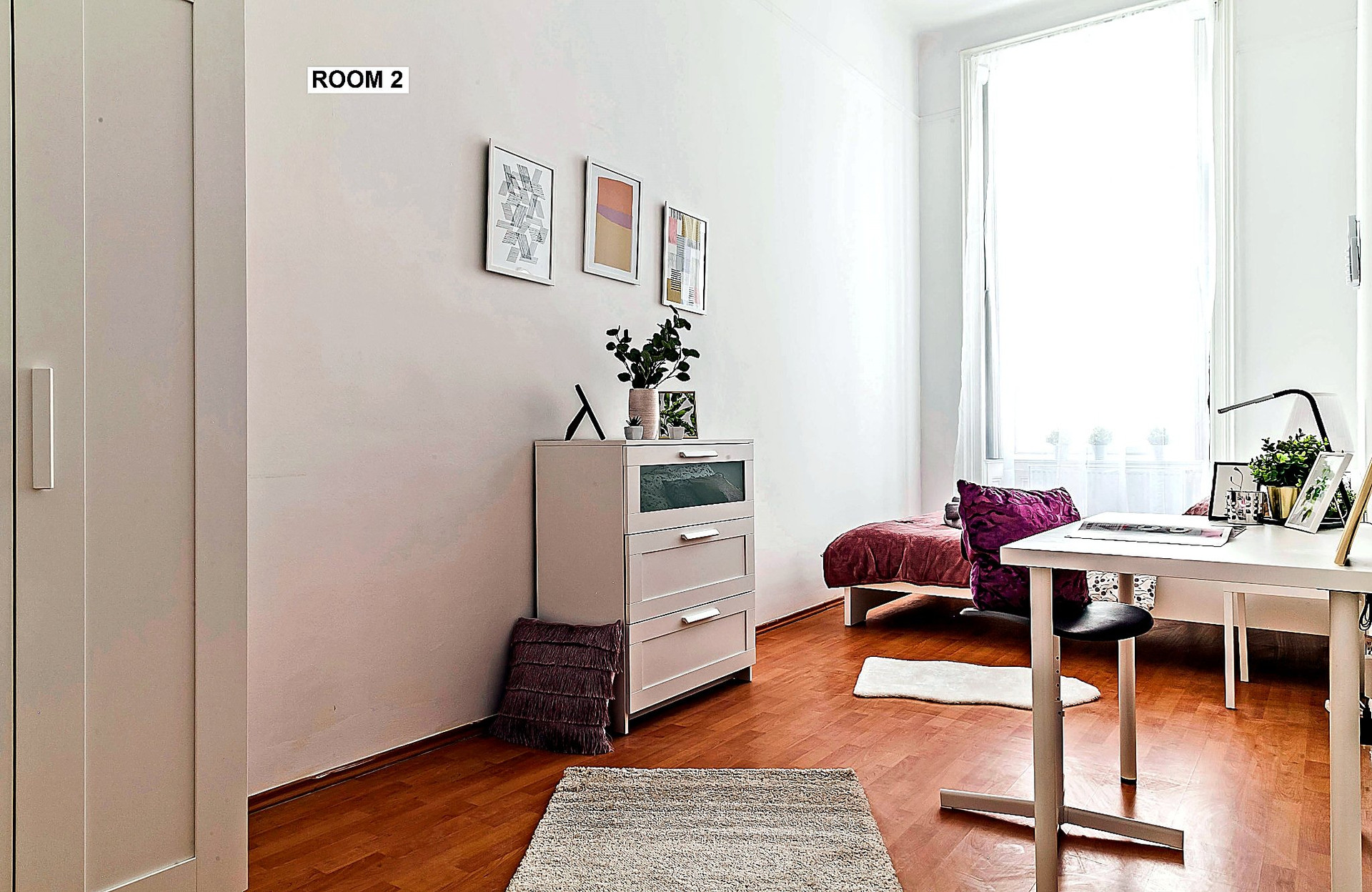 View from the entrance showcasing the room's spacious layout, comfortable furnishings and dedicated work area designed for remote work and study.
