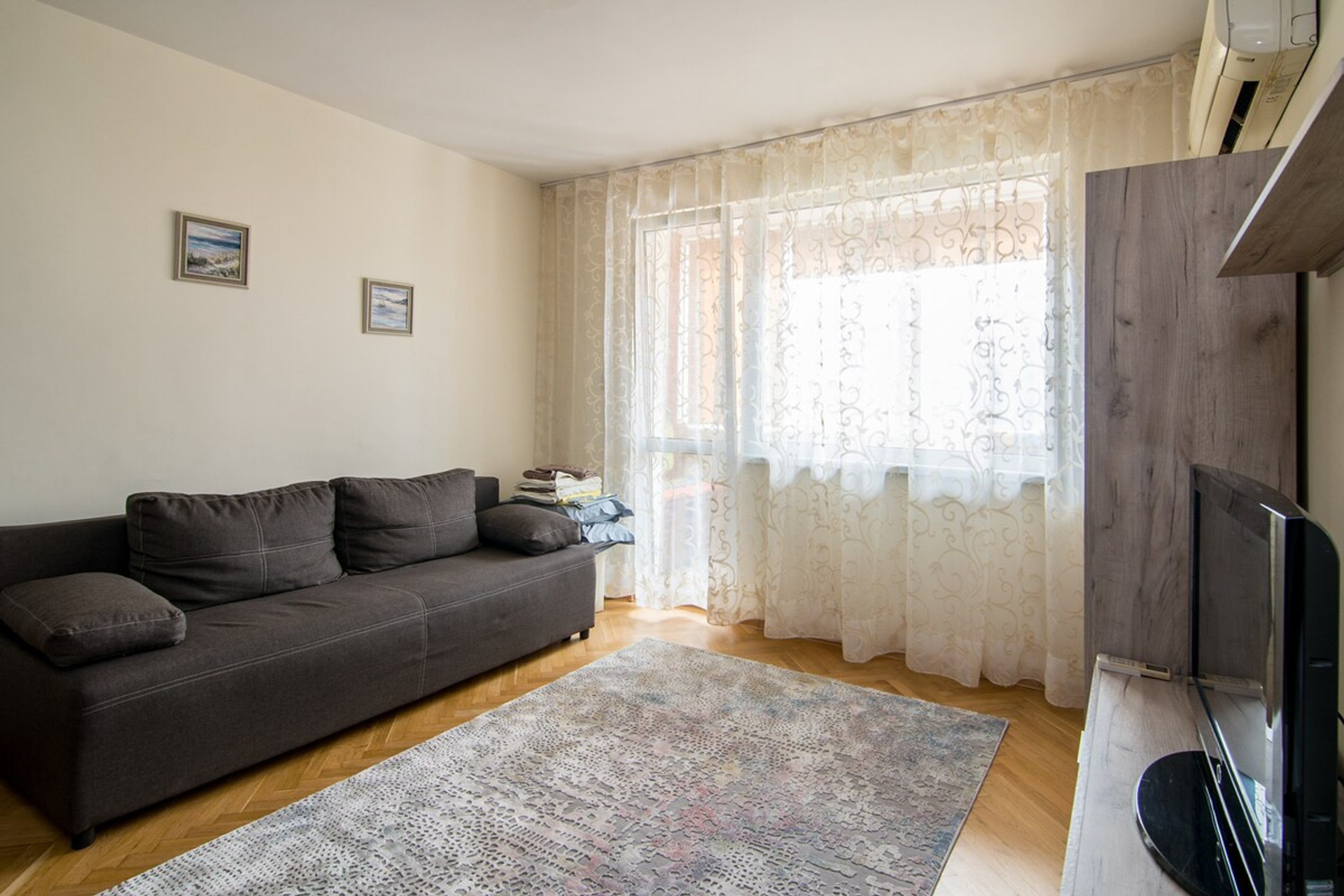 Spacious living room with natural light – A cozy and stylish lounge area featuring a comfortable sofa, large windows, and soft curtains. The perfect space to unwind after a day exploring Varna.