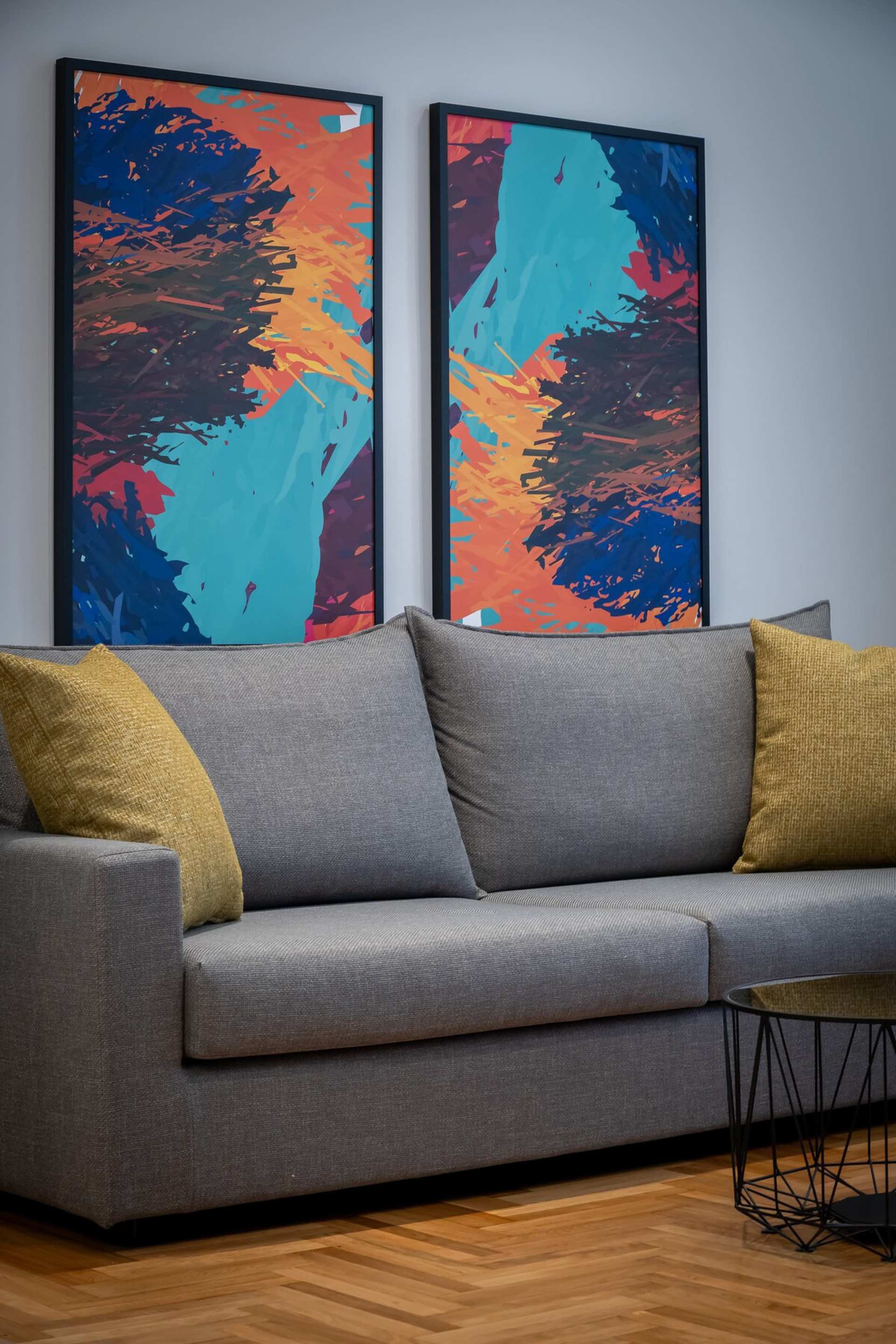 This inviting living area boasts a modern grey sofa adorned with plush mustard cushions, set against a backdrop of vibrant abstract art. The striking artwork adds a splash of colour, creating a cosy yet contemporary atmosphere perfect for relaxation.
