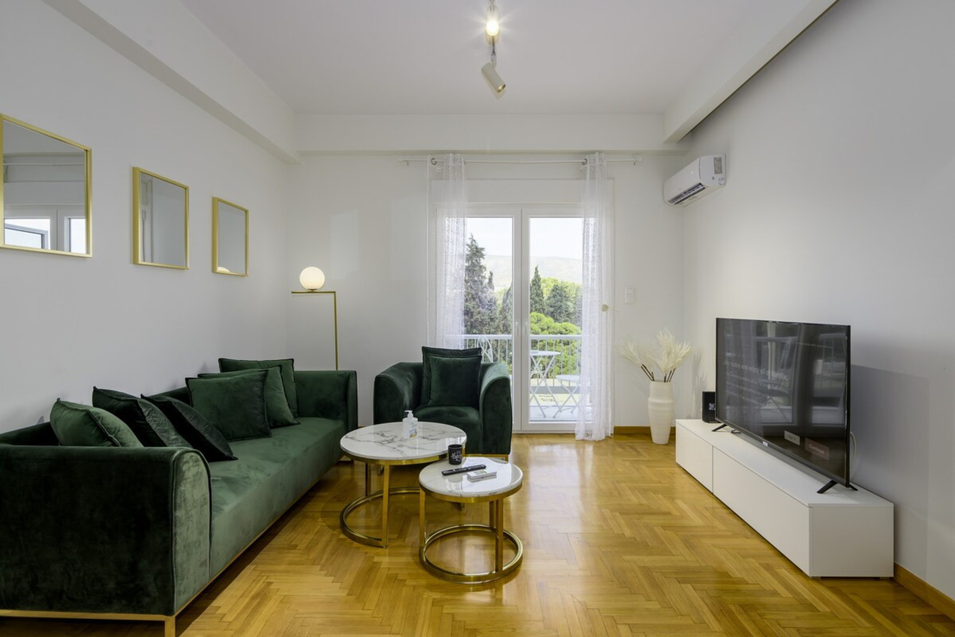 Bright and spacious living room featuring elegant green velvet sofas, modern décor, a smart TV, and large glass doors opening to a serene view. Perfect for relaxing or entertaining in style.