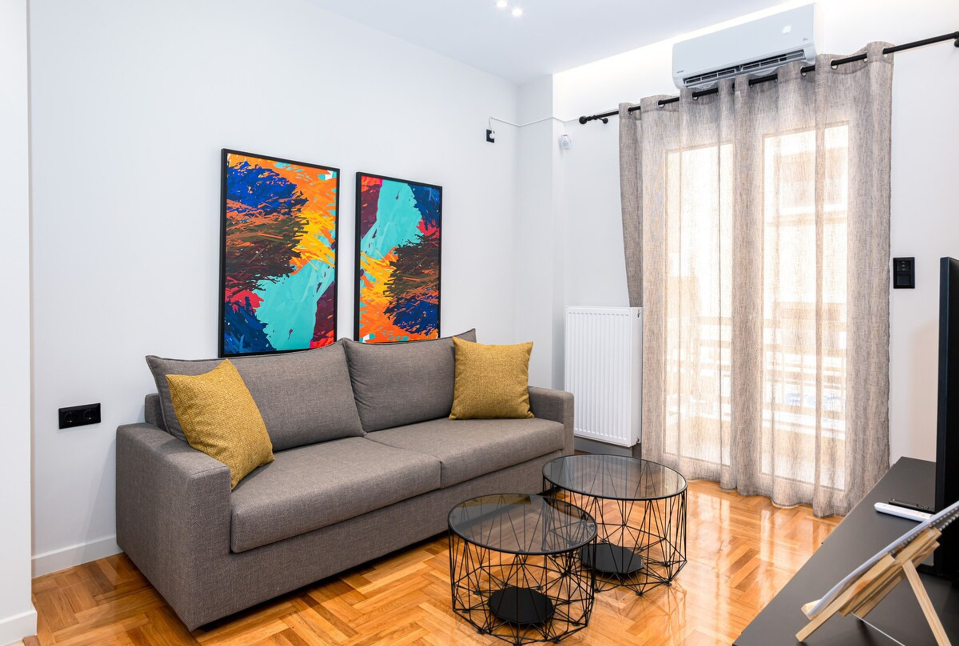Experience comfort and style in this modern living room, featuring a chic grey sofa adorned with vibrant cushions. The space is enhanced by contemporary artwork and ample natural light, creating a welcoming ambience perfect for relaxation.