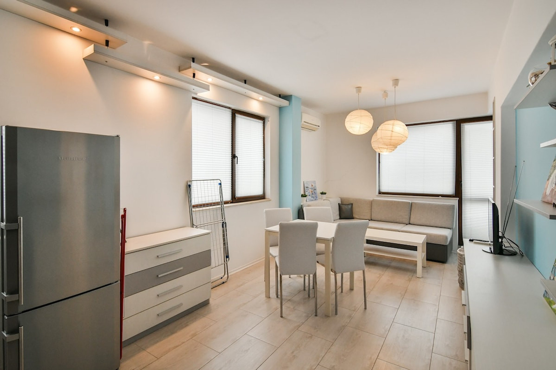 Bask in natural light in this bright, airy living-dining space featuring floor-to-ceiling windows, stylish lighting, and modern decor. Enjoy a comfy sofa, sleek dining table, and a tranquil ambiance—perfect for relaxing or entertaining in central Var