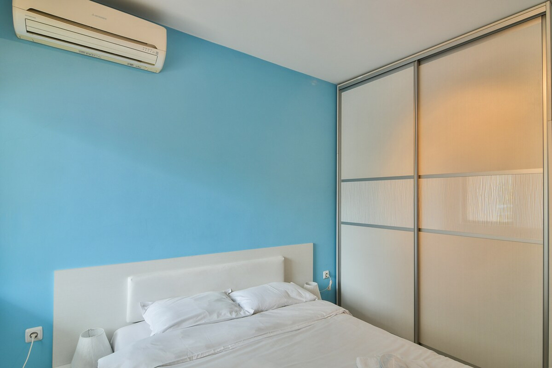 A well-lit and cozy bedroom with contemporary decor, air conditioning, and a comfortable bed. Designed for a restful stay with a peaceful ambiance and natural light streaming through the large window