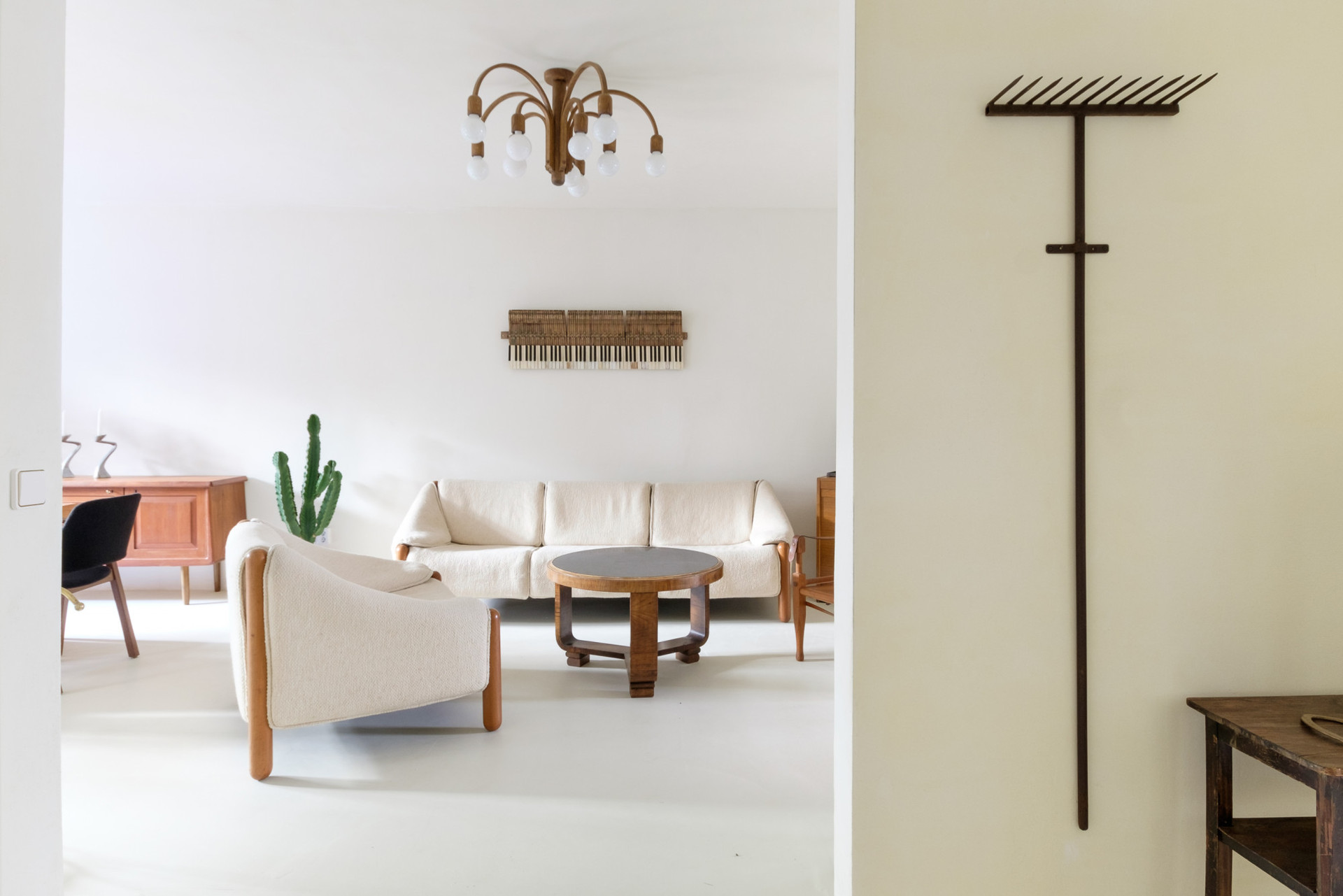 Curated pieces of furniture that have a story to tell: upcycled old piano parts on the living room wall, mid-century wooden chandelier suspended from the ceiling, and an upcycled old rake used as hooks at the entrance