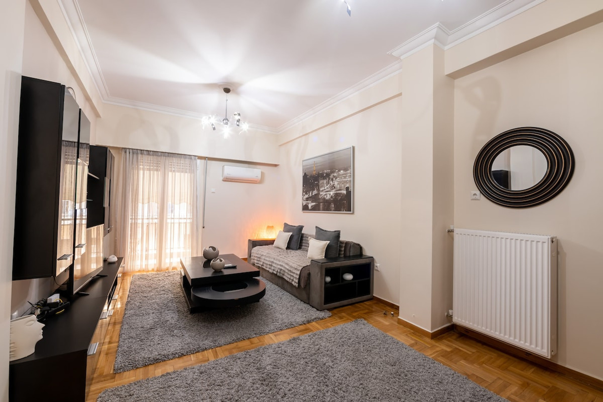 Bright and inviting living room with modern furnishings, cosy sofa, stylish décor, and soft lighting. Features a sleek TV setup, large mirror, and a warm ambience perfect for relaxation. Natural light streams through elegant curtains onto a plush rug