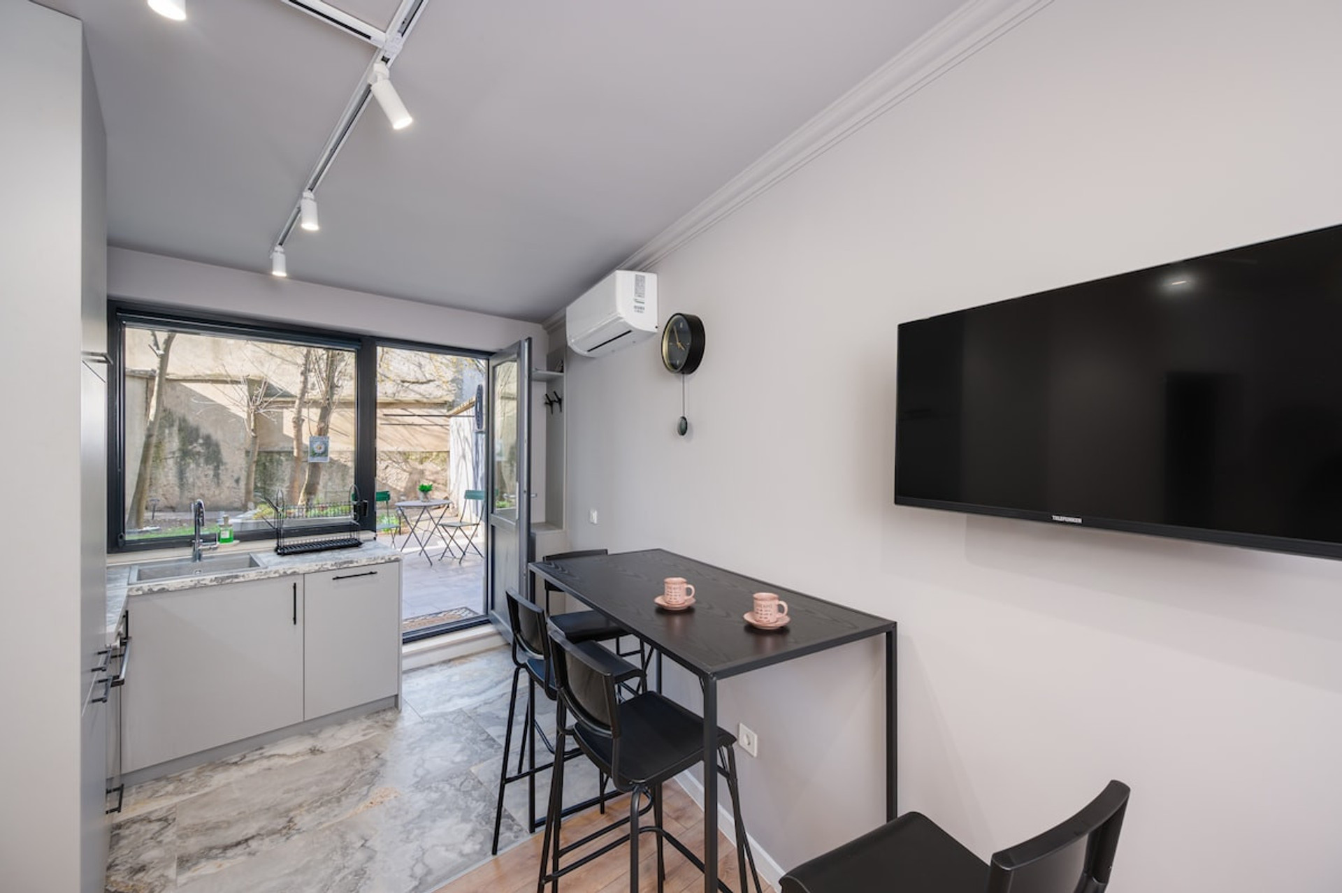 Sleek dining space with a mounted flat-screen TV, natural light, and a view leading to the private patio.