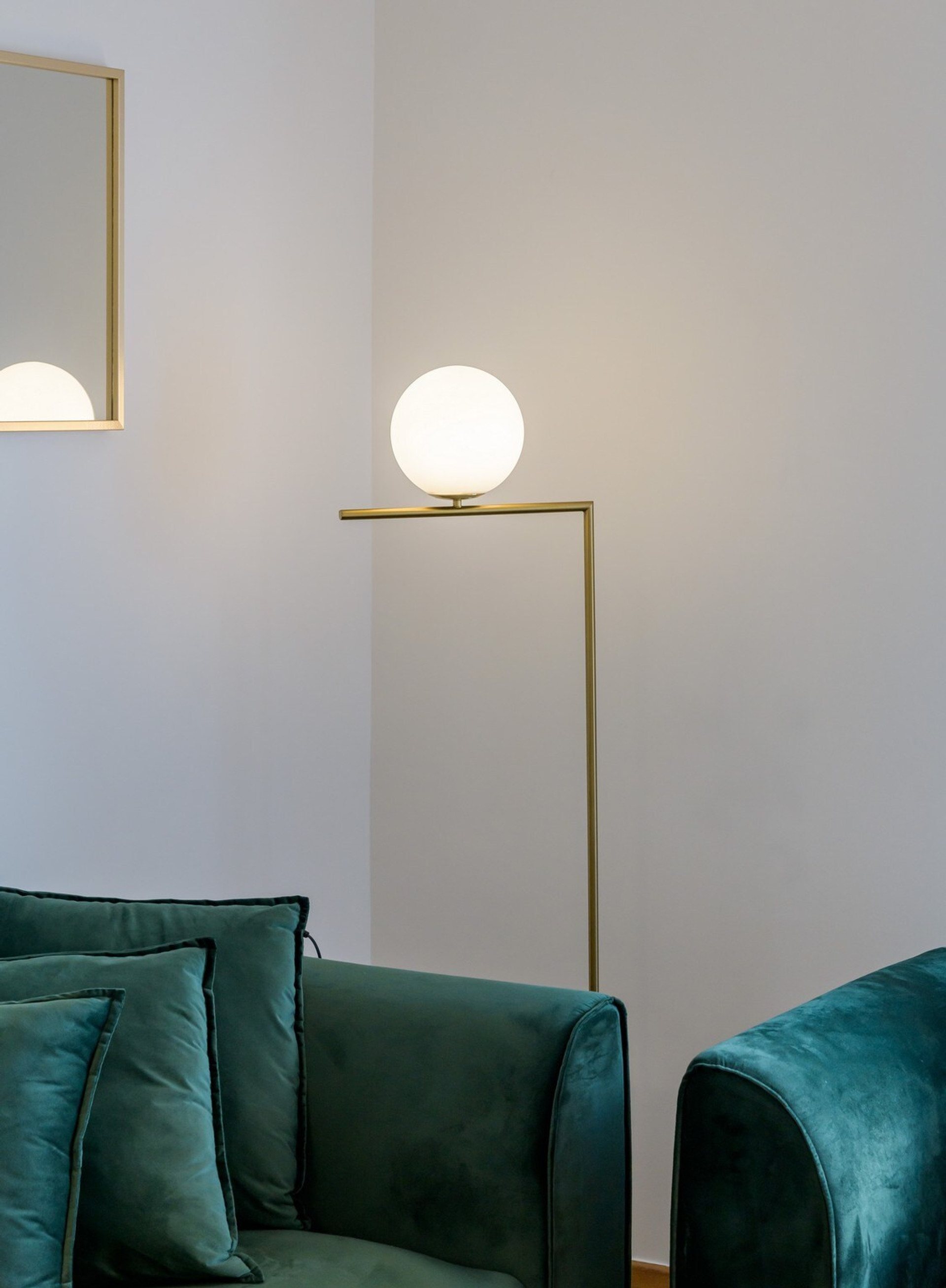 Elegant living space featuring plush emerald green seating, accented by a sleek gold floor lamp with a globe light. The modern design and cosy atmosphere create a perfect spot to unwind.