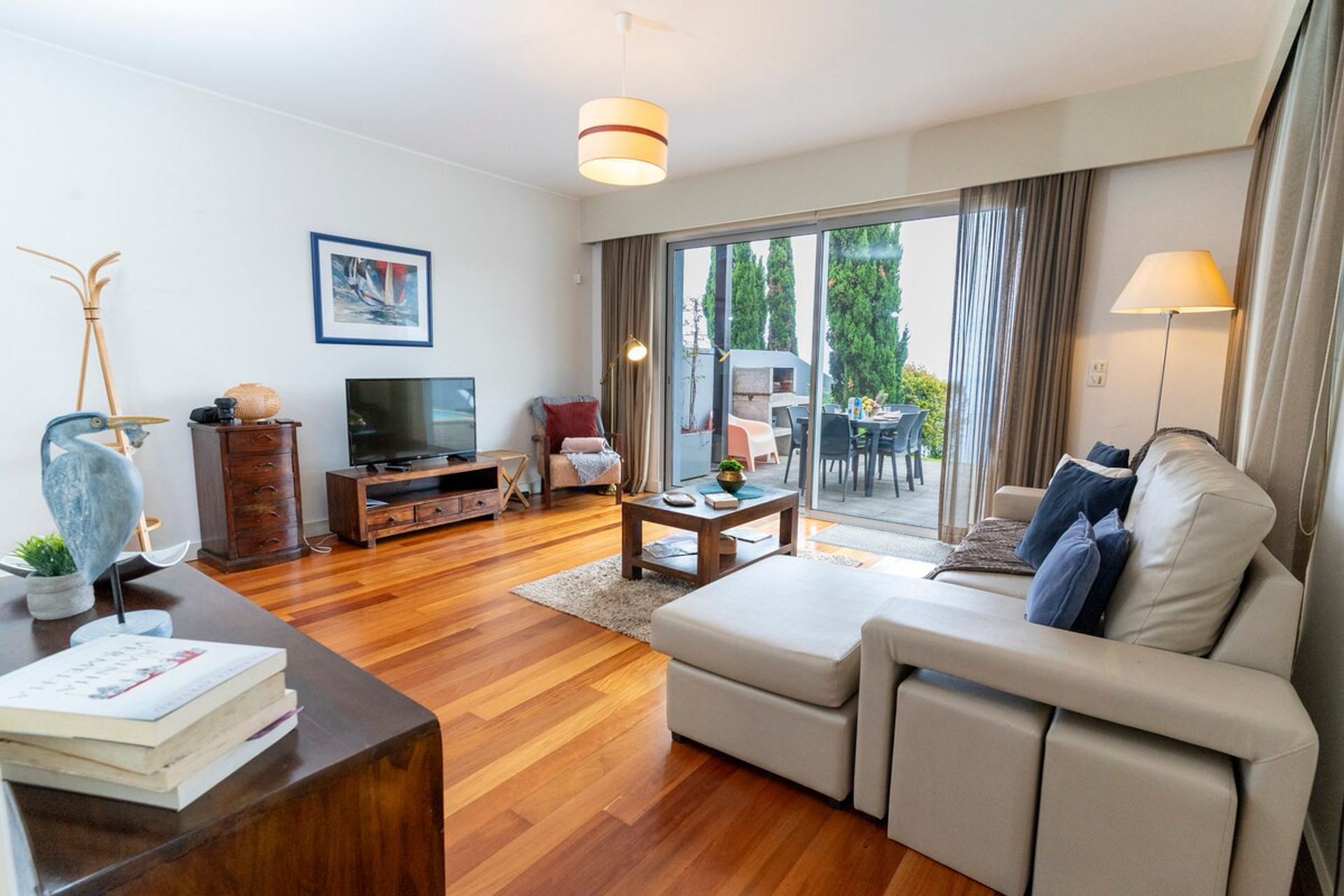 A bright living room with an L-shaped sofa, TV, wooden floor and access to a furnished terrace, creating a cozy and perfect space to relax.
