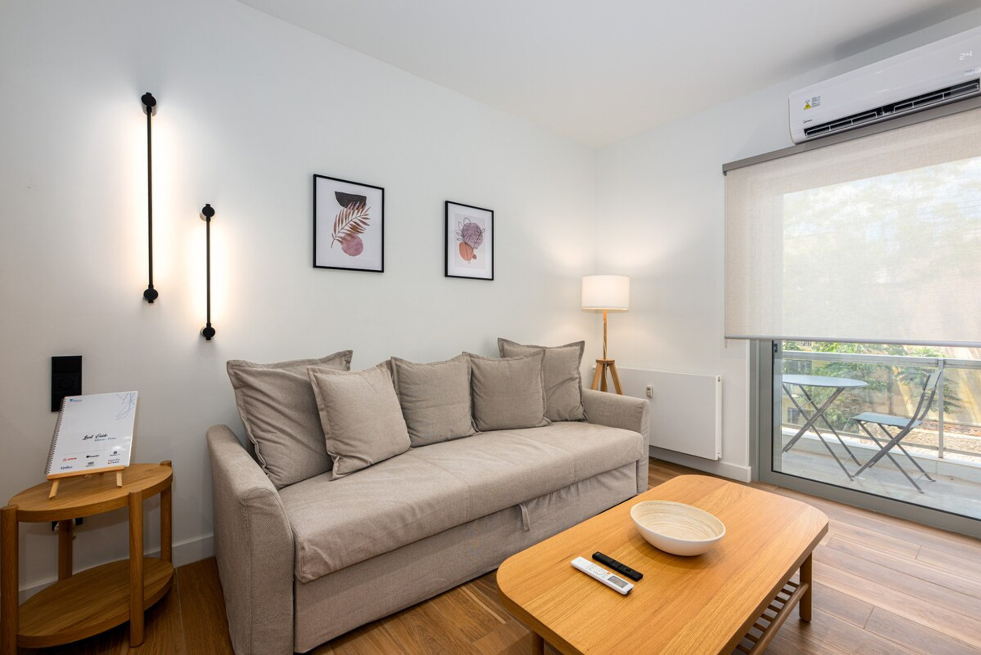 Cosy and stylish living area featuring a comfortable sofa adorned with soft cushions, warm lighting, and elegant wall art. The space opens to a serene balcony view, perfect for relaxation. A blend of modern charm and inviting comfort awaits you.