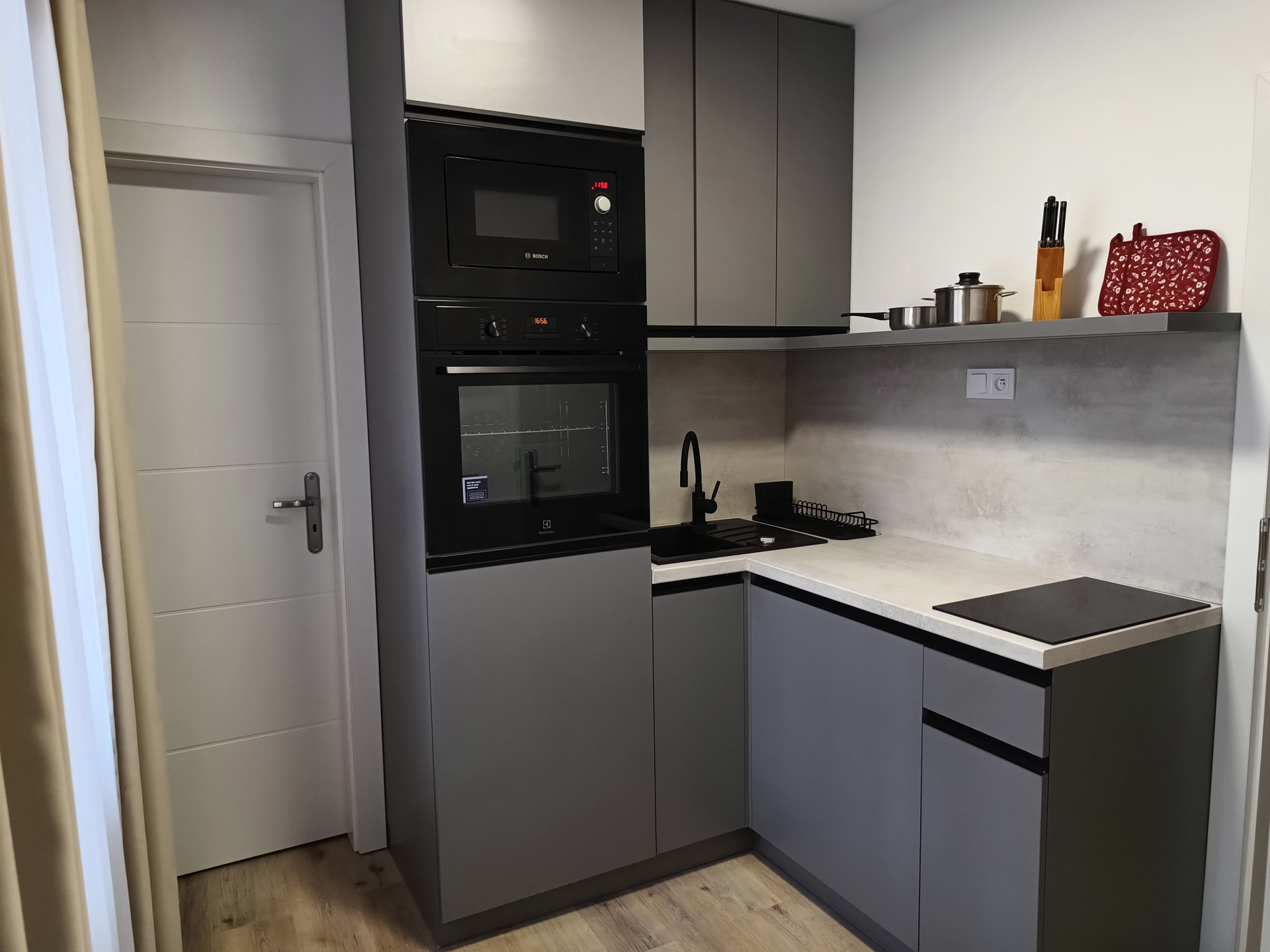 This is the kitchen. The refrigerator is under the oven on the left. The washing machine is under the counter. The door on the left leads to the WC