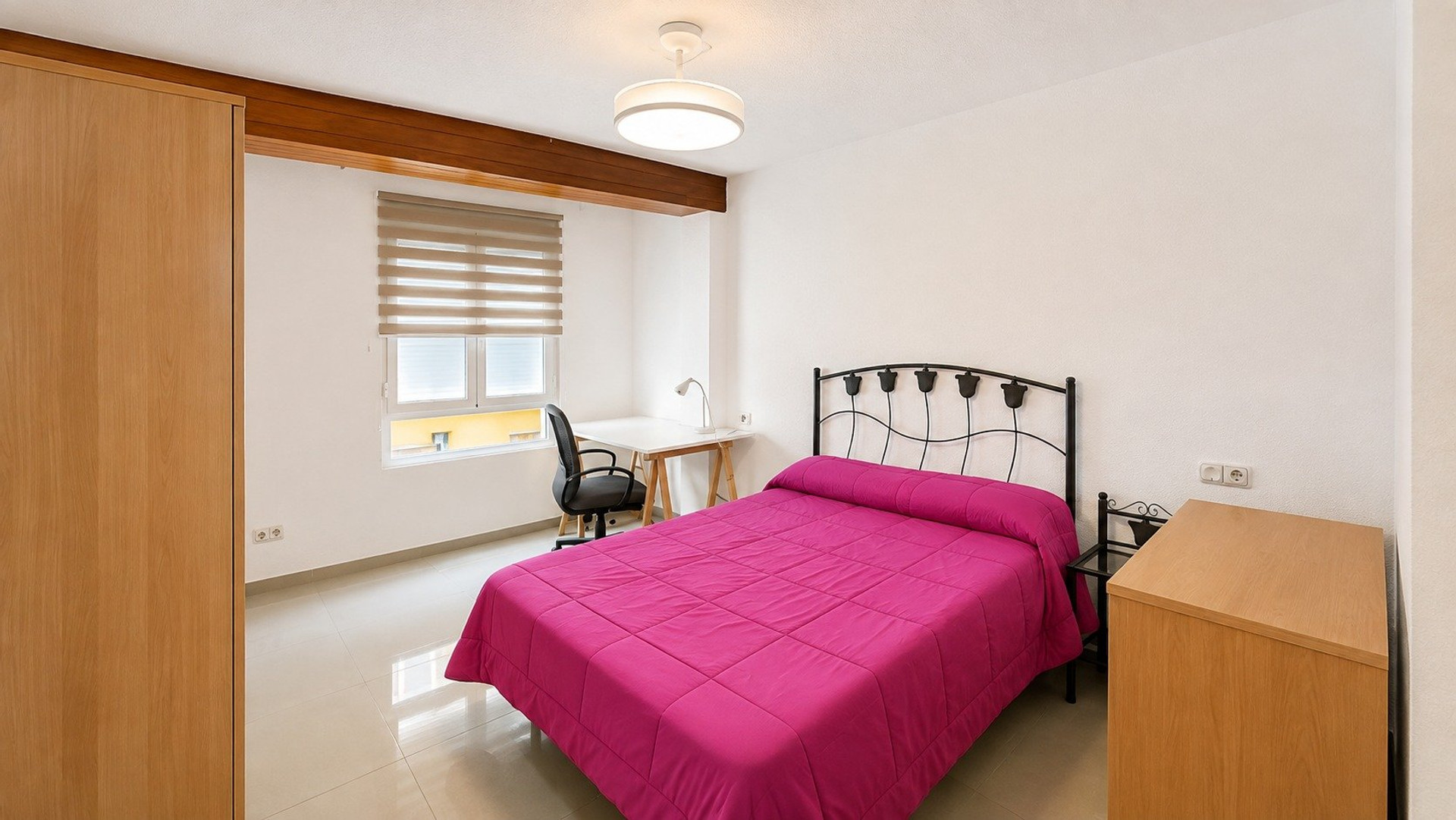 Bedroom with pink bedspread, desk