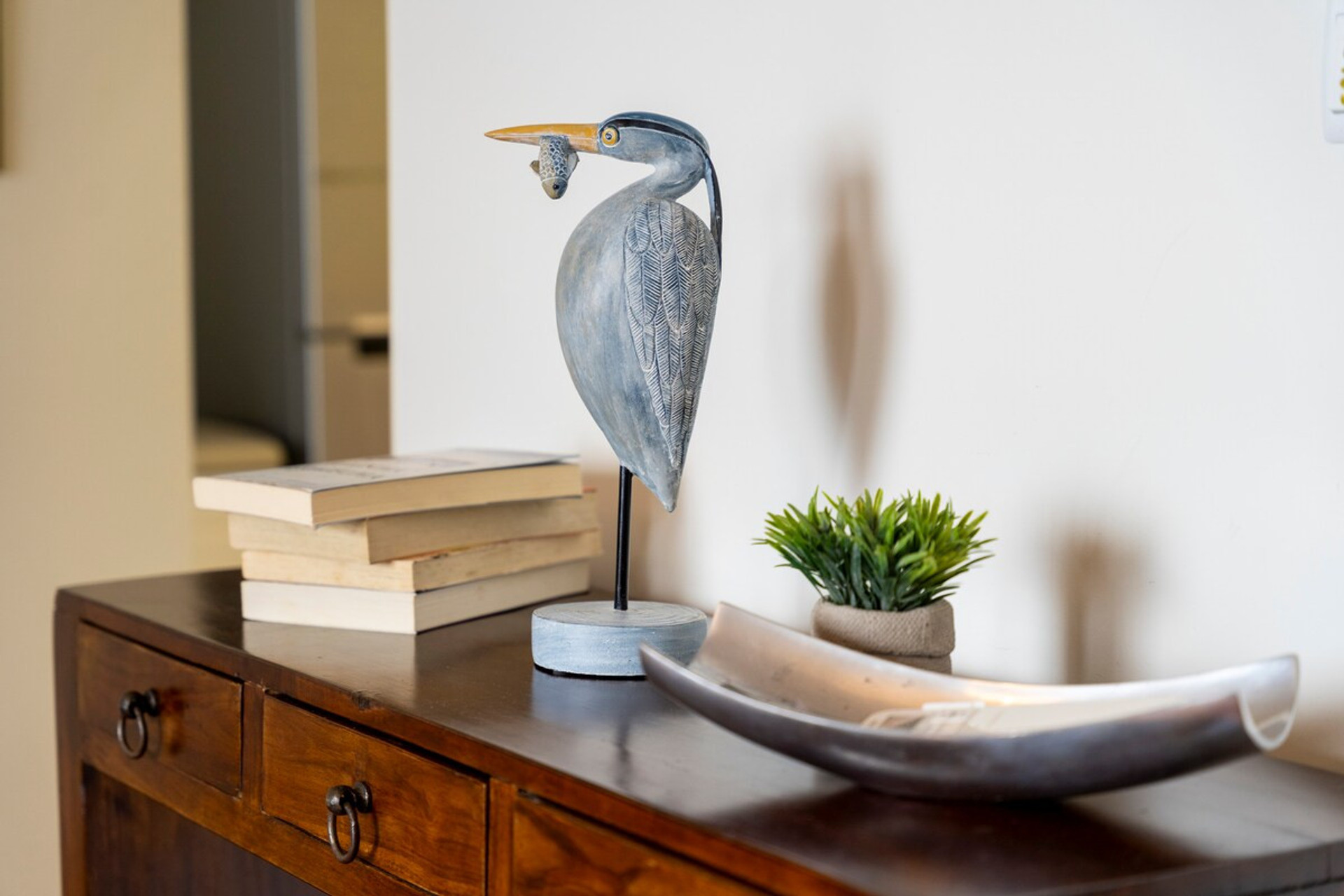 Elegant sideboard with books, bird sculpture, decorative plant, and platter, creating a touch of charm and coziness in the environment.