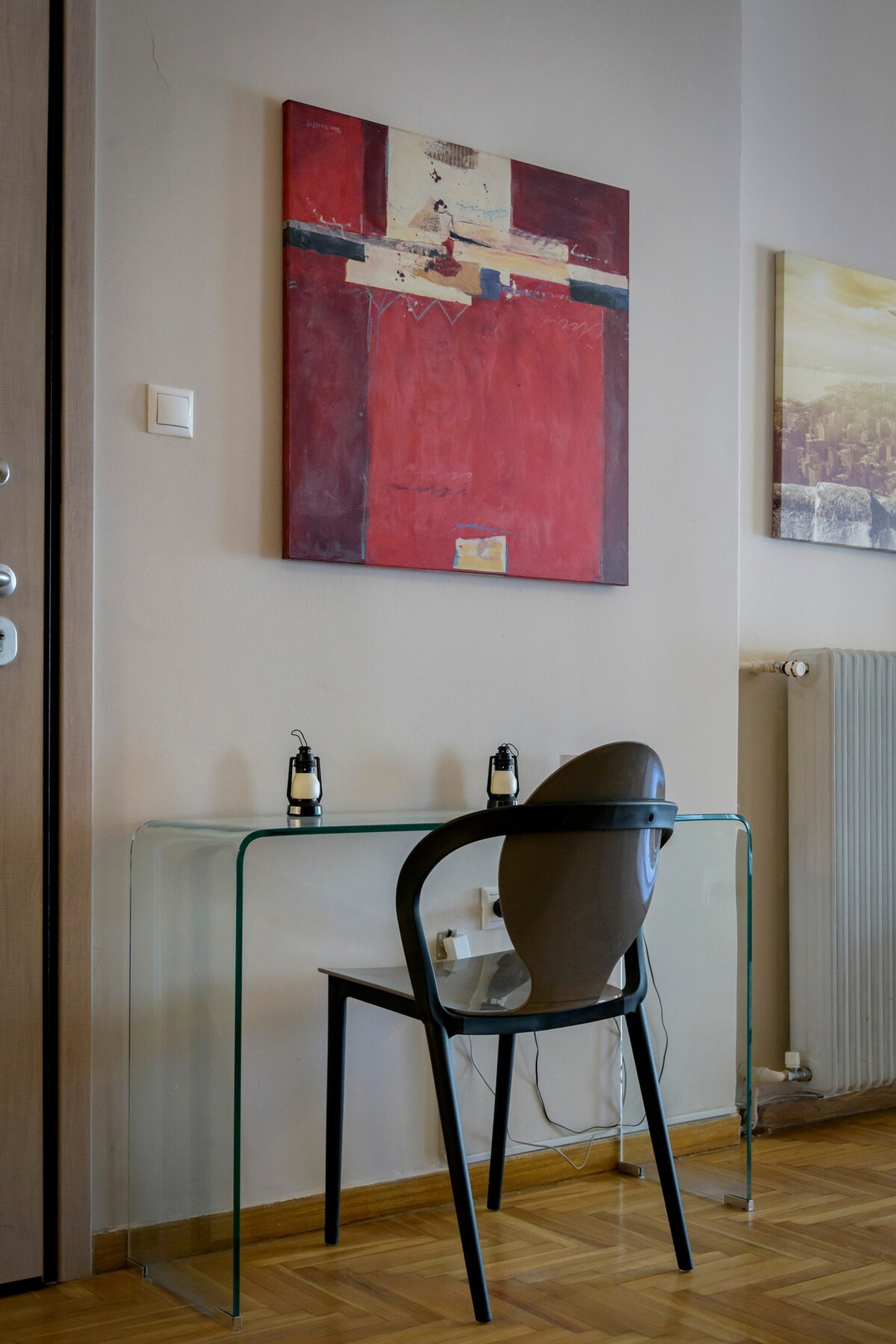 A cosy workspace featuring a sleek glass desk paired with a modern chair, complemented by vibrant artwork that adds character to the room. Perfect for writing, working, or simply enjoying a quiet moment in a stylish and serene setting.