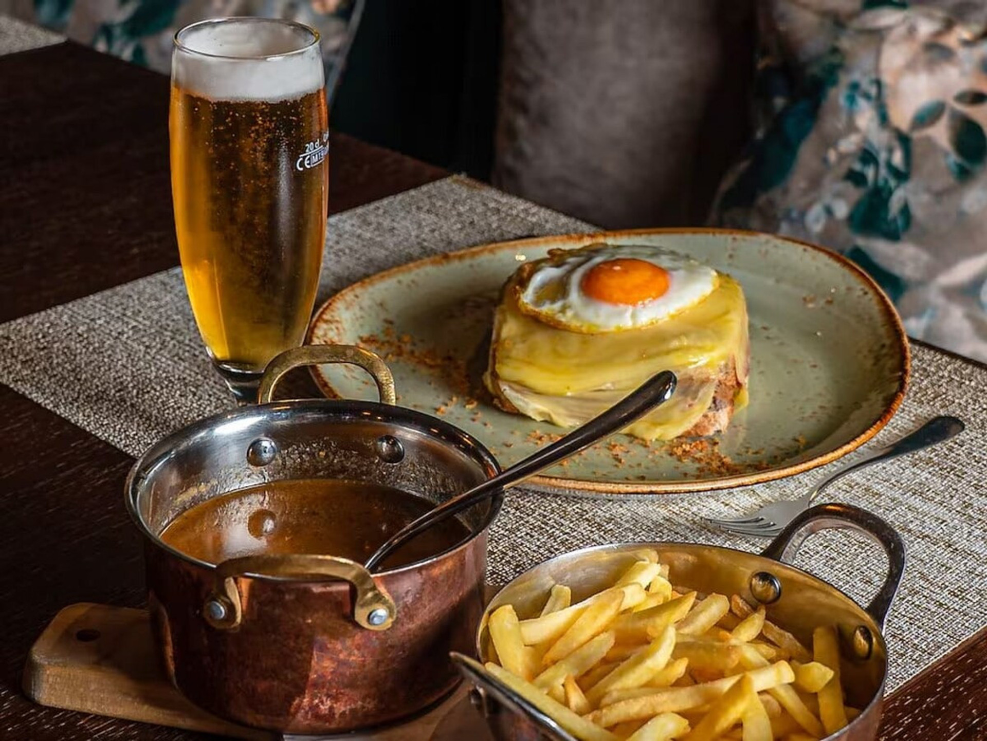 Francesinha sandwich with fries, sauce, and cold beer
