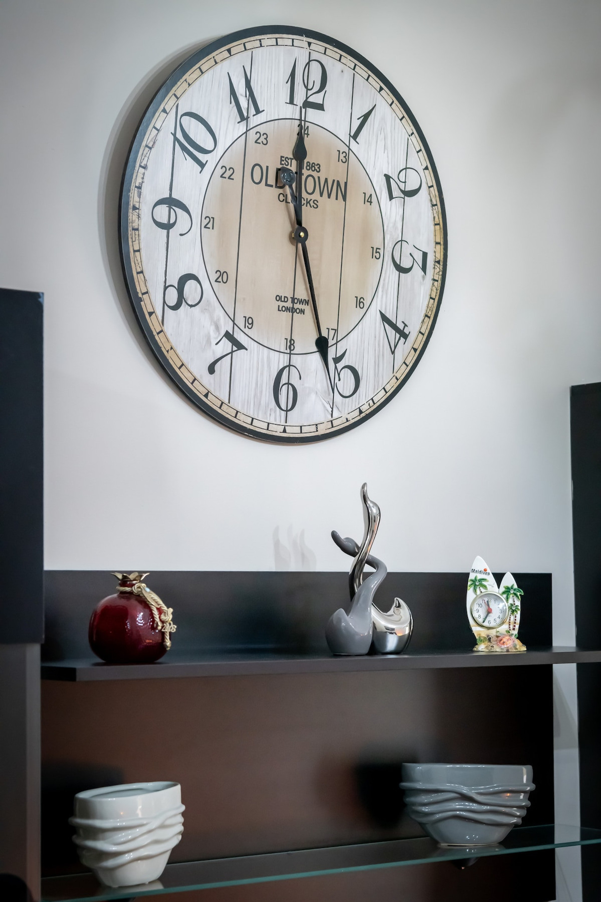 A stylish living room feature with a large vintage-inspired clock as the focal point, complemented by elegant shelves adorned with tasteful decorative pieces, creating a cosy and sophisticated atmosphere for relaxation or entertaining.