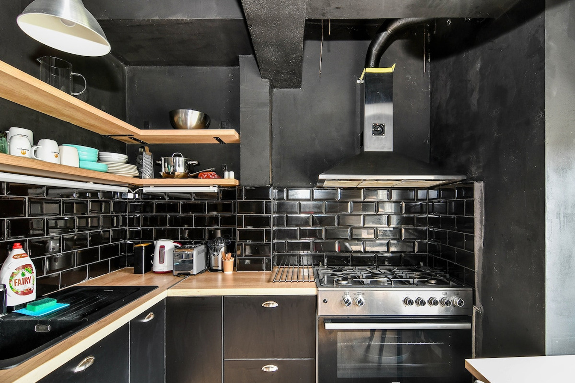 A sleek and contemporary black-tiled kitchen with open shelving and industrial-style accents. Fully equipped for cooking meals during your stay.