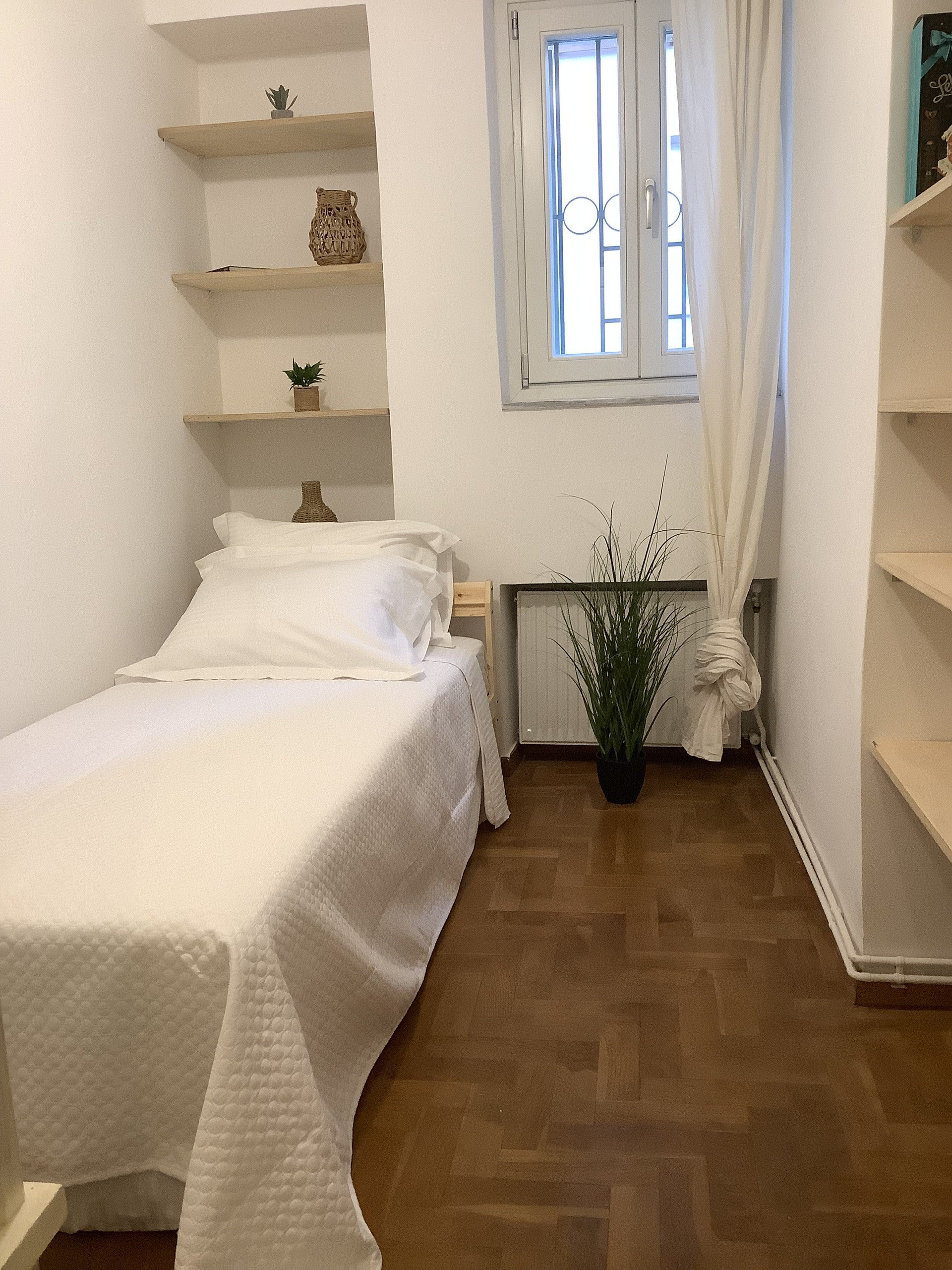 Bright single bedroom with storage shelves and workspace potential.